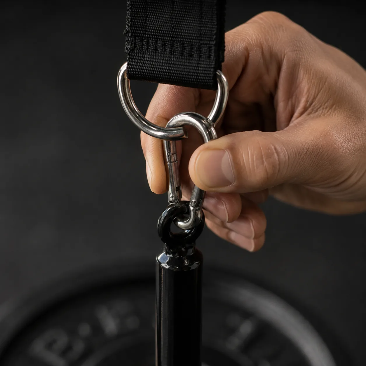 Close-up of a hand clipping the steel carabiner into the black top ring of the loading pin